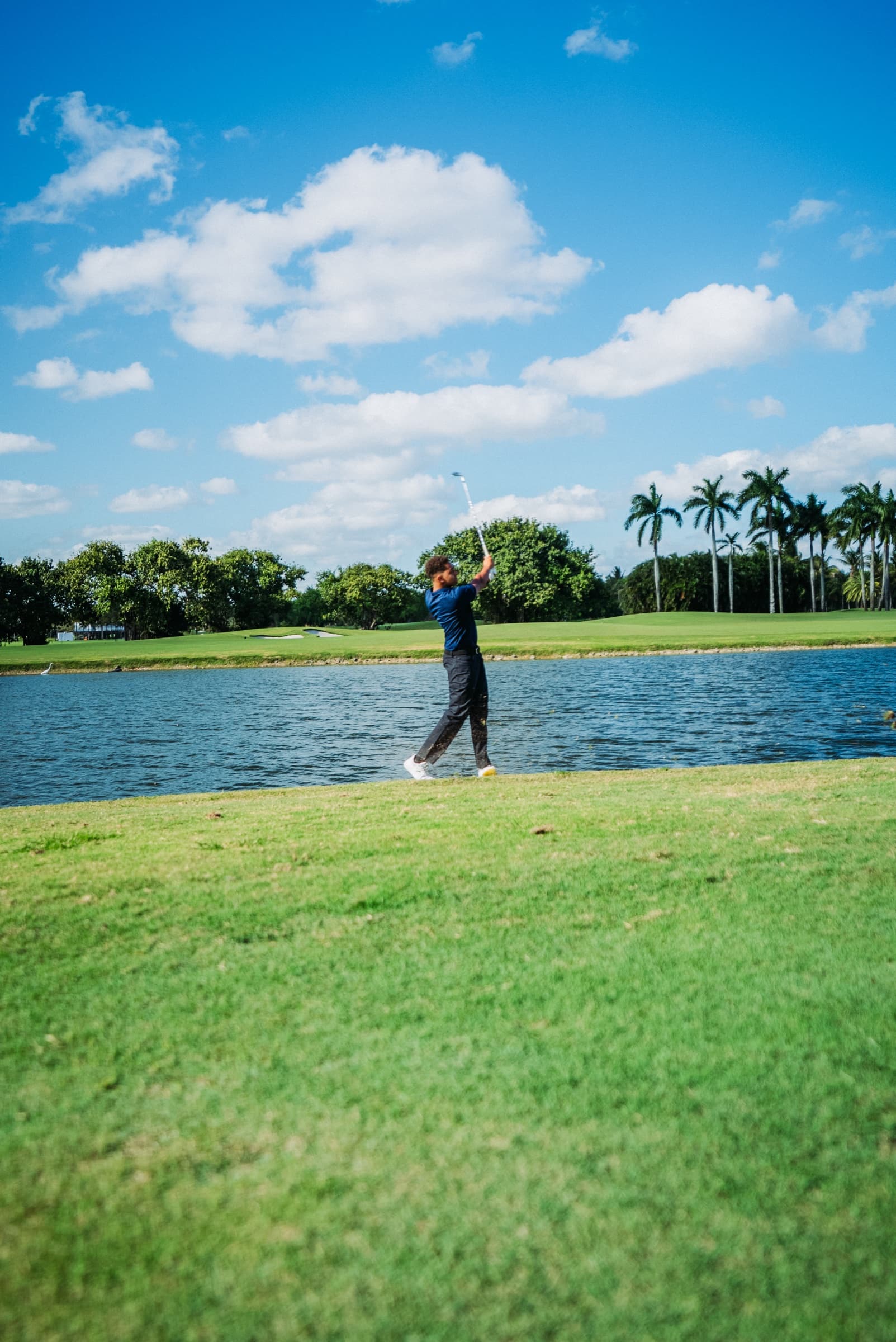 Golfer walking past the pond under scattered clouds