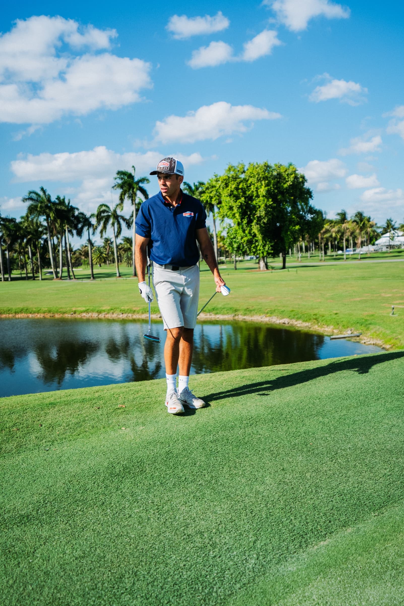 Golfer walking beside a still pond on a palm-lined course
