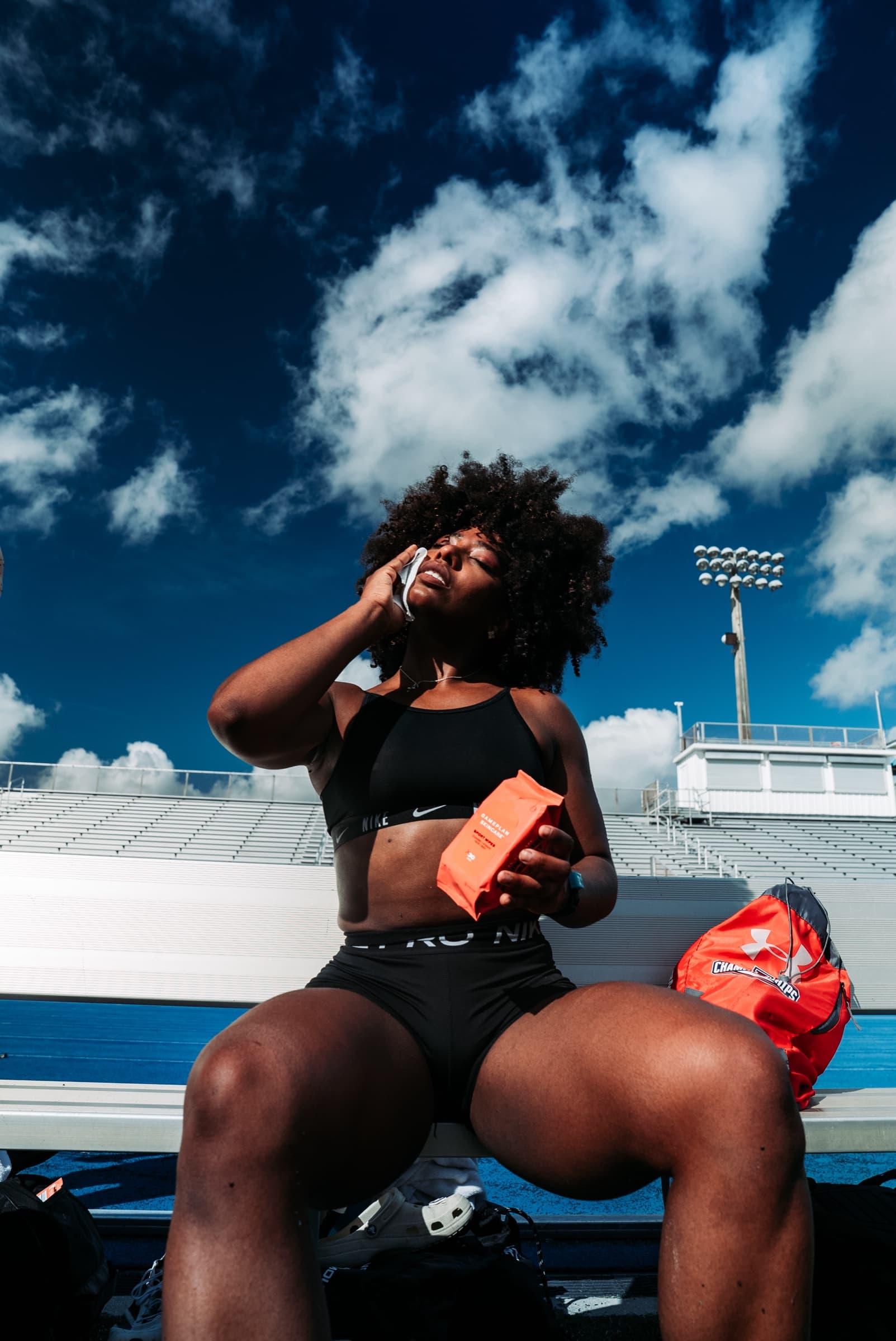 Athlete on a stadium bench, hand to face, against a deep blue sky