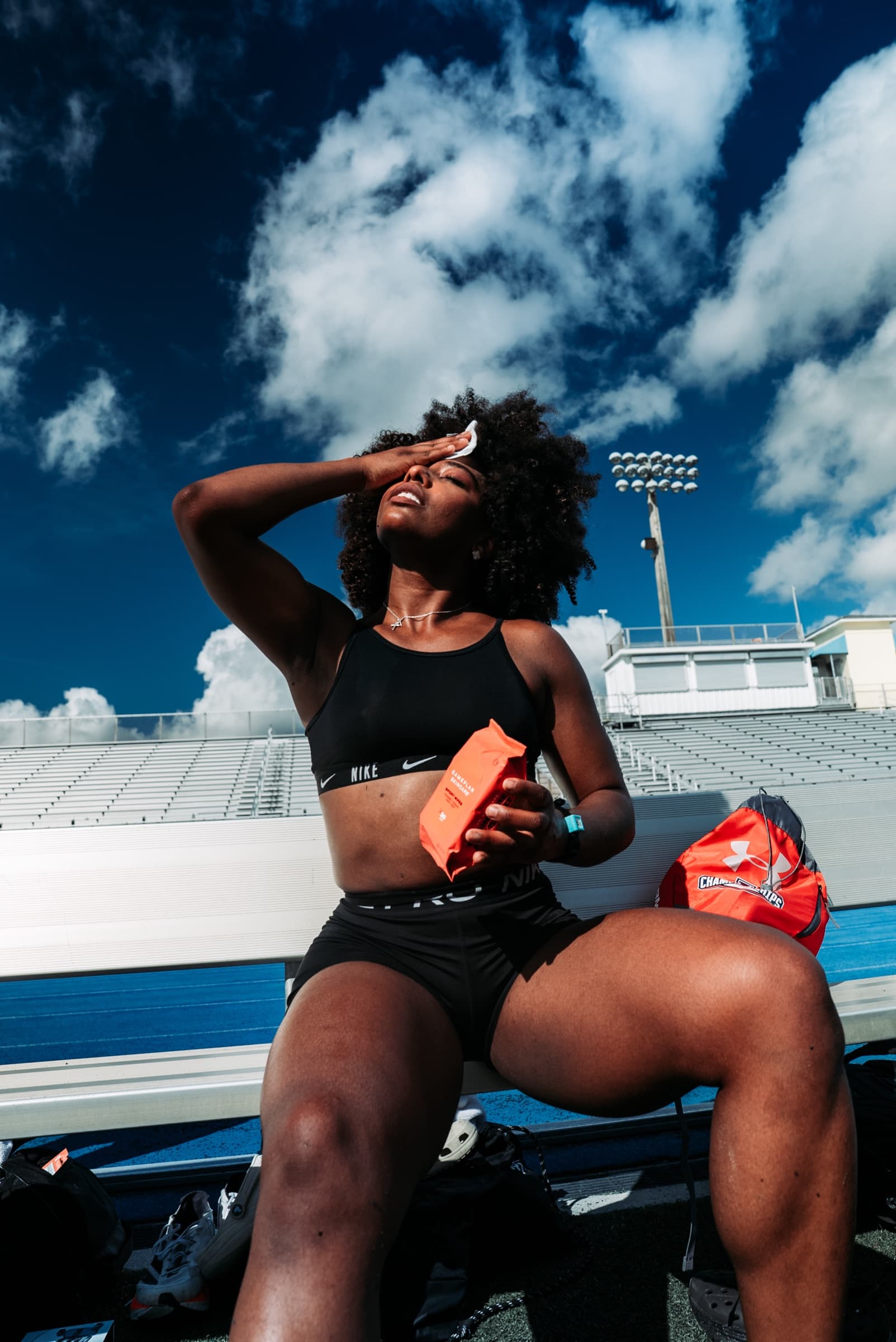 Athlete resting on a bench, hand to forehead, dramatic clouds behind