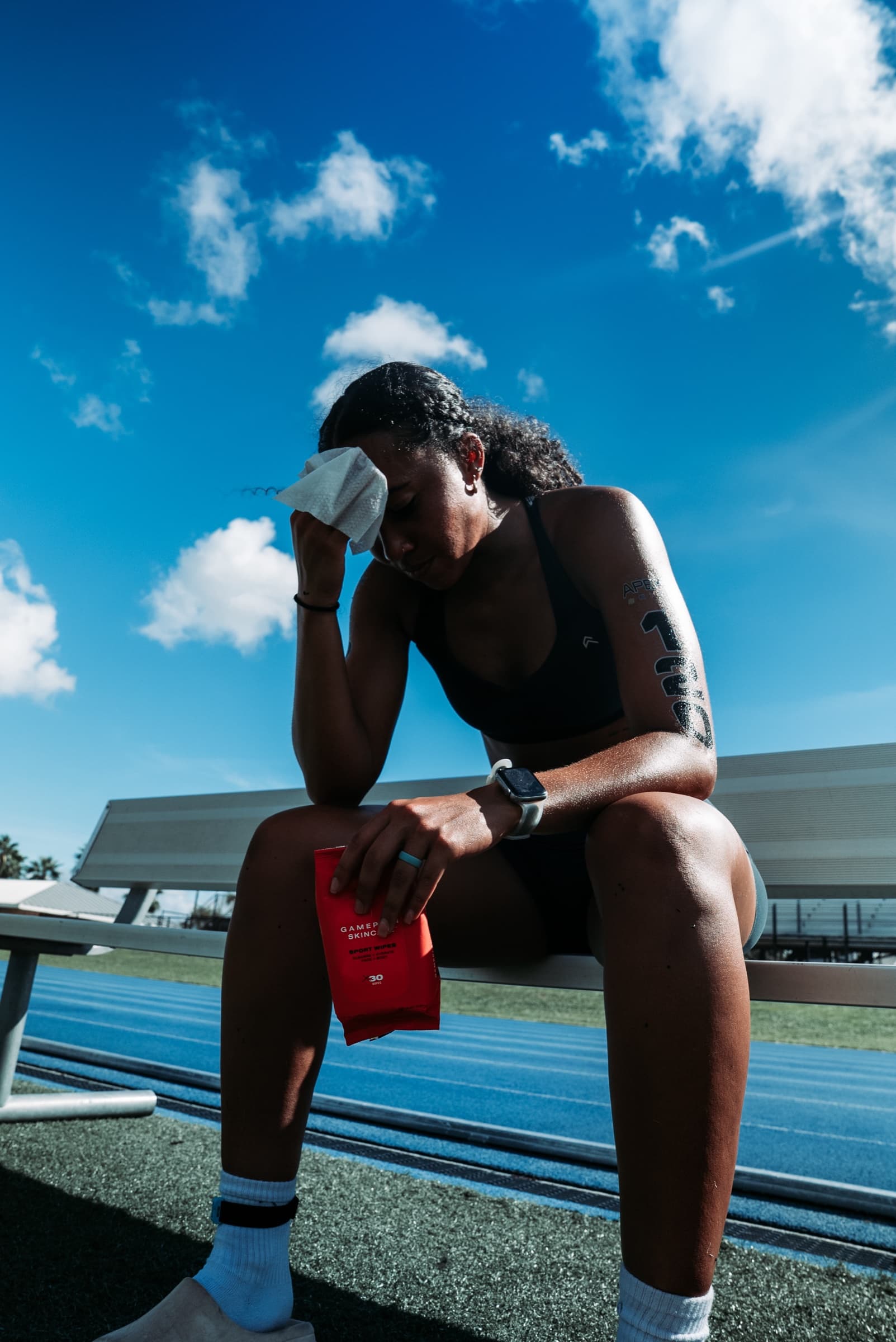 Athlete on a bench, head lowered, wiping their face